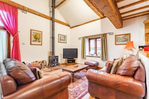 a living room with leather furniture and a tv at Threshers Barn and Shire Horse Barn in Cawston