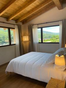 Schlafzimmer mit einem weißen Bett und großen Fenstern in der Unterkunft Casa Rural La Garza y la Paloma in Navaconcejo
