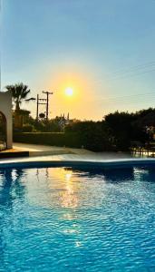 a swimming pool with the sunset in the background at Karteros Hotel in Karteros