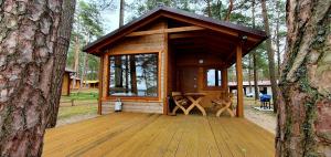 a wooden cabin in the woods with a tree at Domki Borsk - nad samym jeziorem, nowe w pełni wyposażone z miejscem parkingowym in Borsk