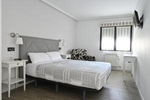 a white bedroom with a bed and a chair at Apartamentos La Cueva - Onis in Avín