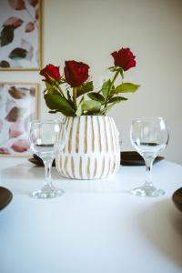Ellafos Traditional Living في Loúkhiou: مزهرية بيضاء مع ورود حمراء فيها بجانب كأسين