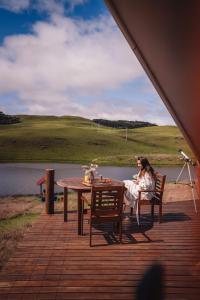 a woman sitting at a table next to a lake at Glamping Atmosphera in Cambará