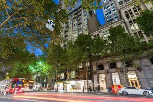 a city street at night with a bus and buildings at A Cozy 2BR Apt on Collins Near Flinders Station in Melbourne