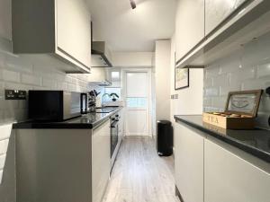 a kitchen with white cabinets and a black counter top at ArtLounge-2 bed garden Free parking in Enfield Lock