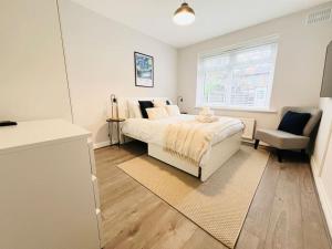 een witte slaapkamer met een bed en een stoel bij ArtLounge-2 bed garden Free parking in Enfield Lock