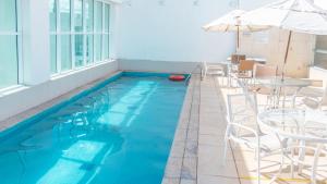 a swimming pool with chairs and a table and an umbrella at Flat2 Saint Moritz in Brasilia