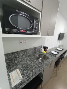 a microwave above a kitchen counter with a sink at Studio completo ao lado do metrô Brás in São Paulo