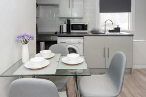 uma cozinha com uma mesa de vidro com cadeiras e um lavatório em Modern 1BR Haven Central Croydon em Croydon