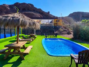 una piscina con mesas de picnic y una sombrilla de paja en Cabañas Caleta Hueso, en Taltal