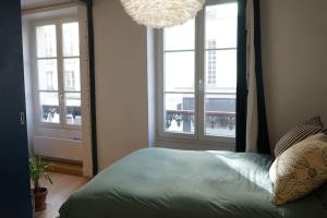 een slaapkamer met een bed, 2 ramen en een kroonluchter bij Appartement au cœur du Marais in Parijs