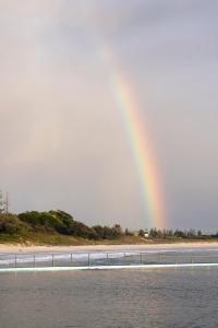 a rainbow over a beach with a bridge and water at Reflections Forster Beach - Holiday Park in Forster