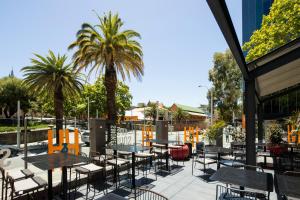 a patio with tables and chairs and palm trees at Mercure Perth On Hay in Perth