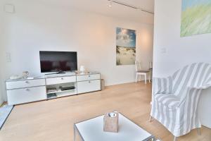 a white living room with a tv and a chair at Orange Hygge Haus in Langeoog