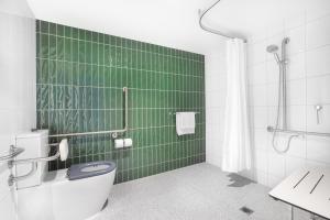 a green tiled bathroom with a toilet and a shower at Holiday Inn Dandenong, an IHG Hotel in Dandenong