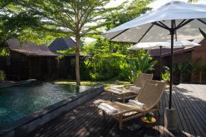 una terraza con 2 sillas y una sombrilla junto a la piscina en Kayu Village, en Canggu