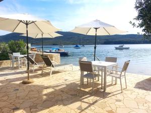 un groupe de tables et de chaises avec parasols à côté de l'eau dans l'établissement Apartman Solis, à Cres