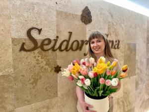 Una donna che tiene un mazzo di fiori davanti a un cartello di Hotel Seidorf w Sosnówce koło Karpacza a Sosnówka