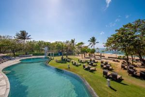 a pool at a resort with lounge chairs and the ocean at MERUSAKA Nusa Dua in Nusa Dua