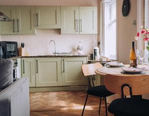 a kitchen with green cabinets and a table with a bottle at Pebble View - Central Cosy with Sea-Views in Weymouth