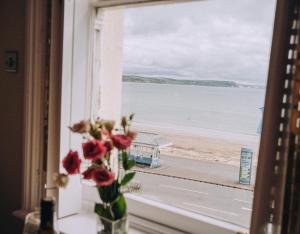 a vase of flowers sitting on a window with a view of the beach at Pebble View - Central Cosy with Sea-Views in Weymouth