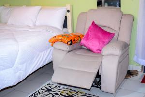 ein Schlafzimmer mit einem Bett und einem Stuhl mit Kissen in der Unterkunft Upper Haven Apartment in Kakamega