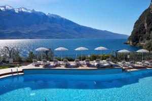 una piscina con sedie e ombrelloni di fronte a un lago di Hotel Atilius a Limone sul Garda