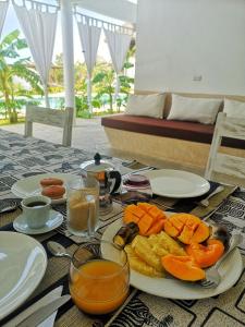 a table with a plate of fruit and juice on it at Mwezi - Maisha Resort in Watamu