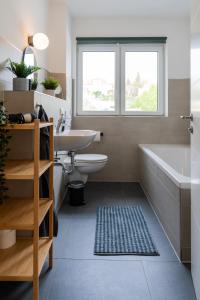 een badkamer met een wit bad, een wastafel en een bad tubermott bij Moderne & Familienfreundliche Ferienwohnung am Goitzschesee in Pouch