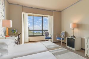 a bedroom with two beds and two chairs and a window at Pestana Bahia Praia Nature & Beach Resort in Vila Franca do Campo
