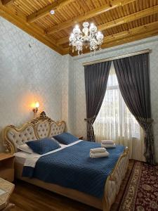 Schlafzimmer mit einem Bett mit blauer Bettwäsche und einem Kronleuchter in der Unterkunft Zilol Baxt Hotel in Samarkand