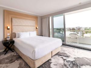 a bedroom with a large bed and a large window at Novotel Sydney Brighton Beach in Sydney