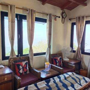 a bedroom with two chairs and a bed and windows at Vineet's homestay in Mukteshwar