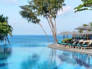 - une piscine avec chaises longues et parasols et l'océan dans l'établissement Pullman Phuket Arcadia Naithon Beach, à Nai Thon Beach