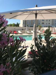 a pool with a white umbrella and chairs and a pool at Mercure Avignon Gare TGV in Avignon