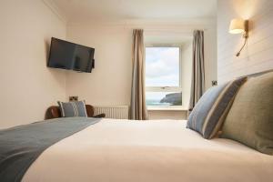 a bedroom with a bed with a television and a window at Port William Inn in Tintagel