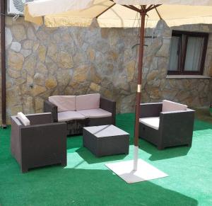 three chairs and an umbrella in front of a stone wall at Casa Gabritana in Sotillo de las Palomas