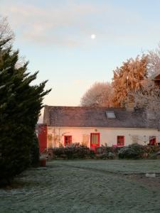 una casa blanca con ventanas rojas y un árbol en Clooncerna Cottage, en Gort