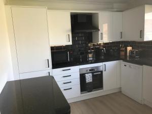 a kitchen with white cabinets and black appliances at Bancroft - Camber Sands - East Sussex in Camber