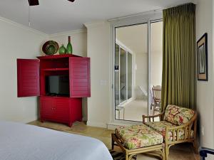 a bedroom with a red dresser with a tv and a chair at Indigo East 1203 in Perdido Key