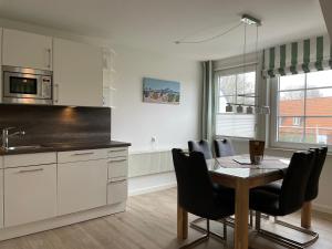 une cuisine avec une table et des chaises et une cuisine avec des placards blancs dans l'établissement Haus am Stadtwald OG Whg 5, Grünstreifen, à Wyk auf Föhr