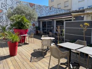 una terraza de madera con mesas, sillas y plantas en Cit'Hotel Le Chêne Vert, en Les Sables-dʼOlonne