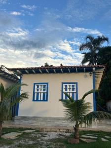 a white house with blue windows and a palm tree at Pousada Rio das Almas in Pirenópolis