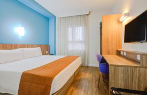 a hotel room with a bed and a desk and a tv at Go Inn Cambuí Campinas in Campinas