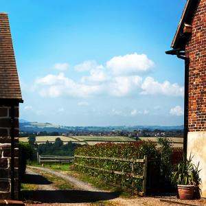 a brick house with a fence and a view of a field at Stone Cottage. Full of character barn conversion Pass the Keys in Highley