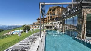 a swimming pool with lounge chairs and a building at Hotel Valentinerhof in Siusi