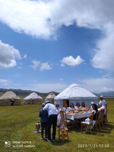 een groep mensen die rond een tafel in een veld zitten bij Zalkar Yurt Camp in Song-Kul