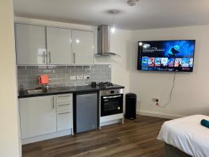 uma cozinha com armários brancos e uma televisão na parede em Elegant Central Luton Studio - Contractors/Airport Travellers! em Luton