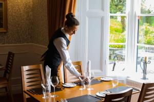 a woman is setting a table in a dining room at Killeen House Hotel in Killarney
