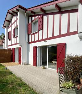 ein Haus mit roten Türen und einer Holzterrasse in der Unterkunft Maison de 2 chambres avec jardin clos et wifi a Briscous in Briscous
